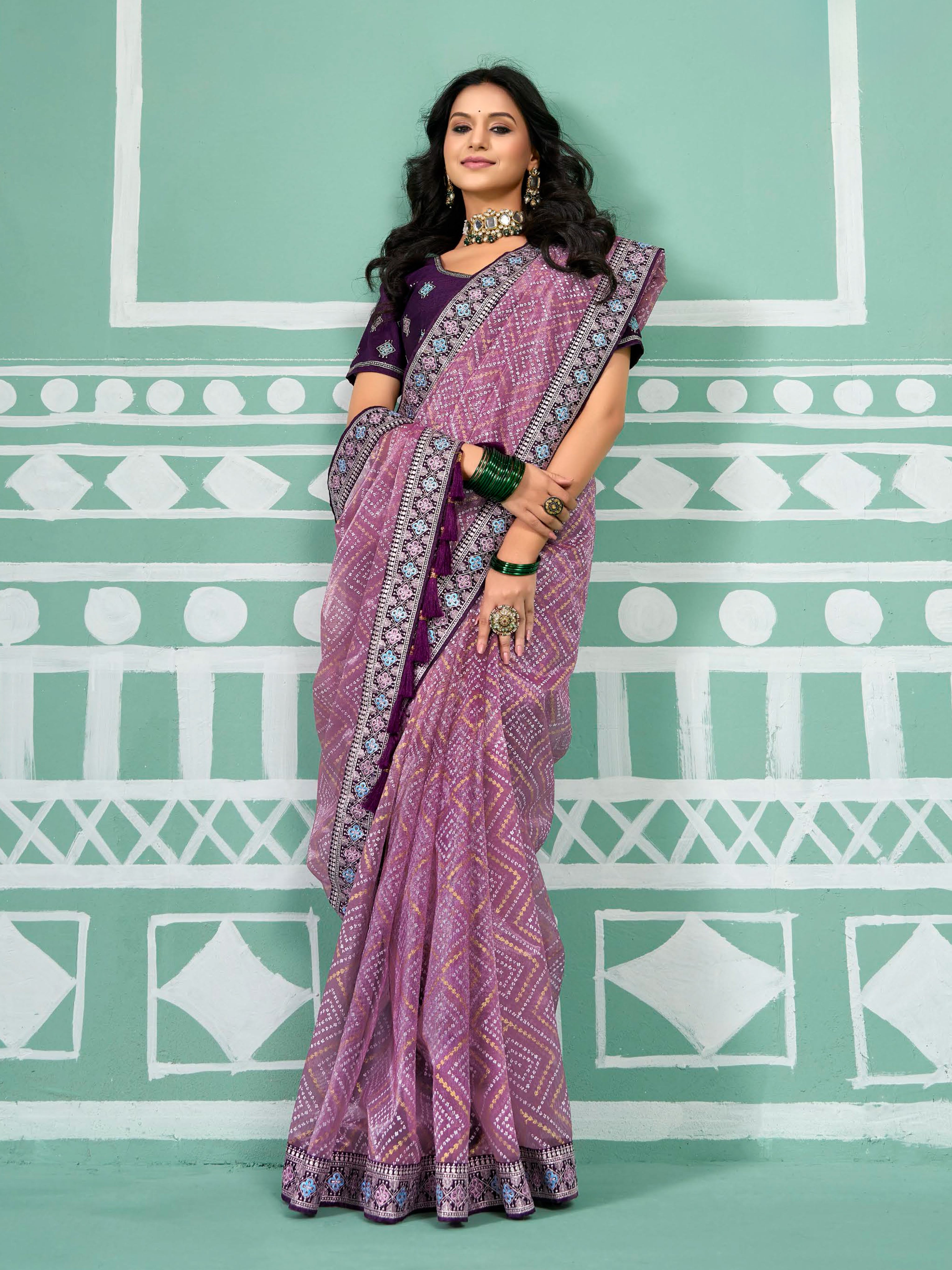 Woman wearing a purple saree with a pattern against a green and white geometric background
