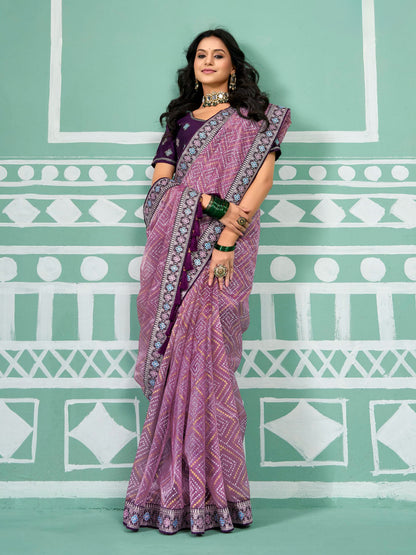 Woman wearing a purple saree with a pattern against a green and white geometric background